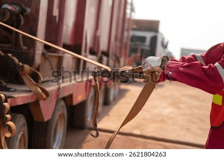 Action of a worker is tightening latching strap belt to secure the load object on trailer truck. Transportation working scene, selective focus.