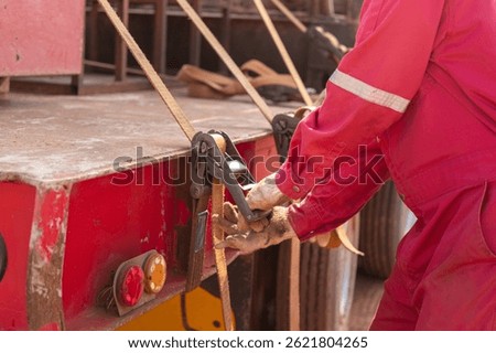 Action of a worker is tightening latching strap belt to secure the load object on trailer truck. Transportation working scene, selective focus.