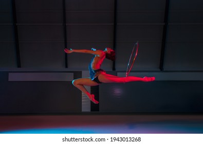 Action. Young flexible girl, rhythmic gymnast practicing isolated over colored background in neon light. Hoop event. Concept of action, motion, sport life, movement, competition. Copy space for ad.