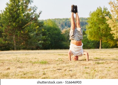 Activ senior man making a headstand in summer in the park