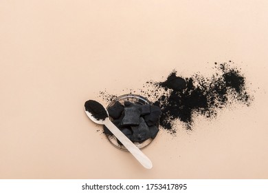 Activated charcoal and wooden spoon on camel color background. Zero waste concept. 