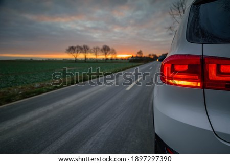 Activated warning lamps on the white car at the emty road in the countryside.