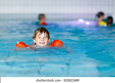 Active Adorable Little Preschool Kid Boy With Swimmies Learning To Swim In An Indoor Pool. Active And Fit Leisure For Children. Happy Child Making Sports And Learning Safe Swimming.