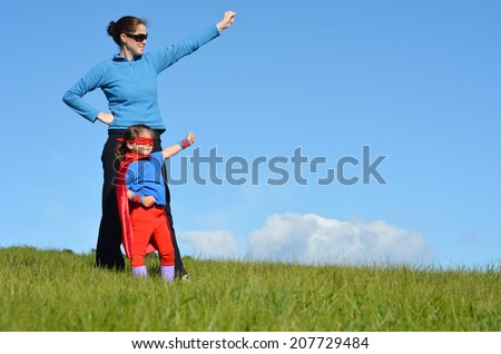 Active adult mother (female age 30) show her young daughter (female age 05) how to be a superhero against blue sky background. Concept photo of Super hero, girl power and gander.Real people.Copy space