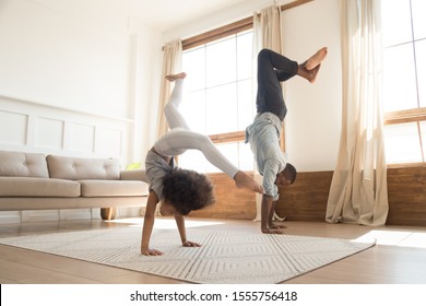 Active African American Young Father And Preschooler Daughter Stand On Hand Exercise At Home Together, Overjoyed Biracial Dad And Girl Child Have Fun Do Morning Gymnastics, Healthy Family Concept