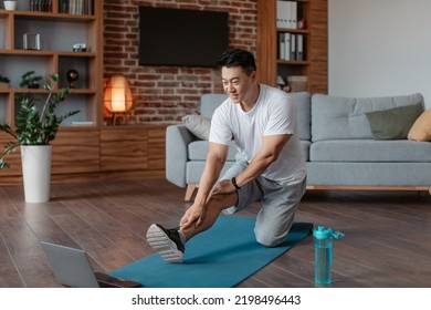 Active asian mature man in sportswear stretching leg muscles in front of laptop, sitting on floor yoga mat, watching online tutorials, warming up before domestic training - Powered by Shutterstock