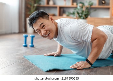 Active asian mature man standing in plank pose or doing push ups on mat at home and smiling at camera. Active korean male leading active lifestyle, exercising indoors - Powered by Shutterstock