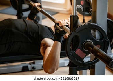 Active Asian sport man in black sportswear lying on exercise bench doing barbell bench press lifting at weightlifting station. Indoor weight training and muscular building workout in fitness gym - Powered by Shutterstock