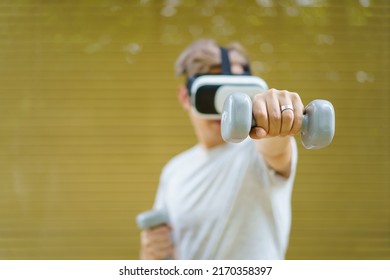 Active Asian Sportsman Doing A Weight Training Exercise By Using Dumbbell And Virtual Reality - VR Goggles Platform For Online Training. The Innovation Of Virtual Reality Or Metaverse Platform Concept