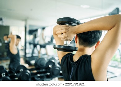 Active Asian sportsman doing a weight training exercise by lifting up a dumbbell, man lifting up or holding a heavy dumbbell in Overhead Tricep Extension position. Bodybuilding workout.