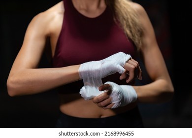 Active Asian woman wraps her hands with boxing bandages while do kickboxing fighting exercise in abandoned building. Healthy strong female athletic do sport workout training alone in dark place - Powered by Shutterstock