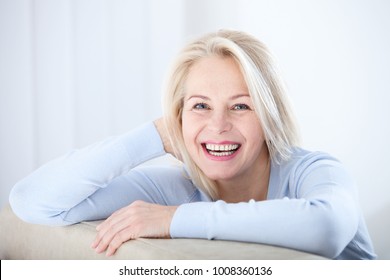 Active beautiful middle-aged woman smiling friendly and looking in camera in living room. Woman's face closeup. Realistic images without retouching with their own imperfections. Selective focus. - Shutterstock ID 1008360136