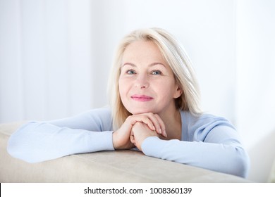 Active Beautiful Middle-aged Woman Smiling Friendly And Looking In Camera In Living Room. Woman's Face Closeup. Realistic Images Without Retouching With Their Own Imperfections. Selective Focus.