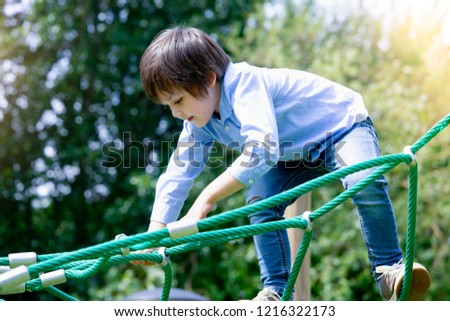 Active boy playing outdoors, 4 Years kid climbing rope at playground in retro filter, Happy child enjoying activity in a climbing adventure park on a summer day