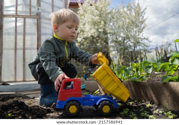 Active boy preschooler with\
blonde hair playing with a plastic truck in the garden. The child\
learns to play without adult supervision. Happy and carefree\
childhood.