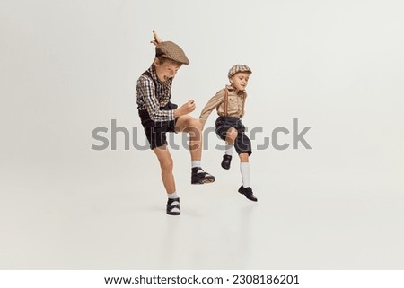 Active boys, children in stylish classical clothes playing together, running, jumping over grey background. Fun. Concept of game, childhood, friendship, activity, leisure time, retro style, fashion.