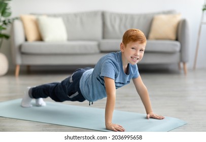 Active caucasian redhead school boy exercising alone at home, doing push-up on yoga mat in the middle of living room, panorama with copy space. Sport, activity, healthy lifestyle for children concept - Powered by Shutterstock