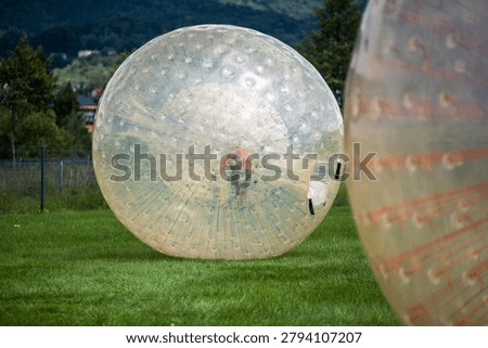 Active child having fun inside a giant inflatable zorbing ball on a green meadow in summer
