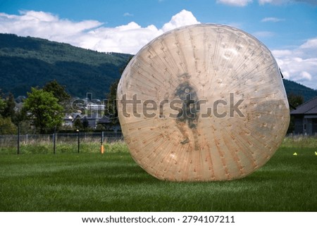 Active child having fun inside a giant inflatable zorbing ball on a green meadow in summer