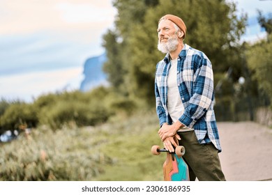 Active cool bearded old hipster man standing in nature park holding skateboard. Mature traveler skater enjoying freedom spirit and extreme sports hobby leisure lifestyle, authentic shot. - Powered by Shutterstock