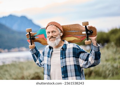 Active cool happy bearded old hipster man standing in nature park holding skateboard. Mature traveler skater enjoying freedom spirit and extreme sports hobby on mountains background. Portrait - Powered by Shutterstock