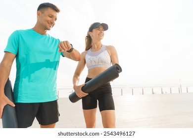 Active Couple Checking Workout Plan Outdoors at Sunrise With Yoga Mats in Hand on a City Terrace - Powered by Shutterstock