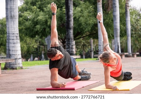 Active couple performing side plank exercise on yoga mats outdoors in a park. Man and woman training together with focus and balance. Concept of fitness, healthy lifestyle, strength, and teamwork.