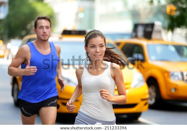 Active couple\
running on famous shopping street fifth avenue in Manhattan, New\
York City NYC, USA. Exercise lifestyle portrait of young asian\
woman runner and caucasian male\
jogger.