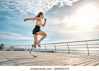 Active disabled woman with leg prosthesis in sports clothing jumping while her morning workout outdoors. Disabled sport concept. Copy space. Full lenght. - Shutterstock ID 2044941572
