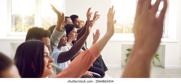 Active diverse multiracial male female audience. Side profile view mixed race multiethnic men and women sitting in row raising up hands to ask coach question after engaging talk, session, master class