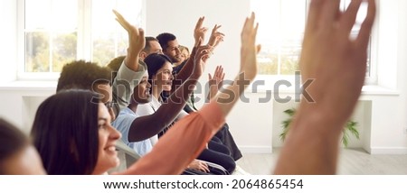 Active diverse multiracial male female audience. Side profile view mixed race multiethnic men and women sitting in row raising up hands to ask coach question after engaging talk, session, master class