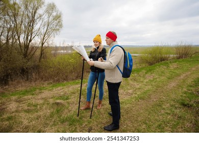 Active elderly Caucasian couple hiking with backpacks and hiking poles enjoying their adventure. They are looking at a map or a tourist route. - Powered by Shutterstock