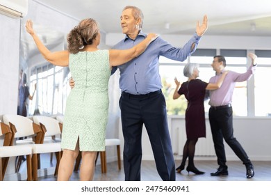 Active elderly couple in their free time is engaged in modern latin dance class and learns movements of cha-cha-cha dance - Powered by Shutterstock