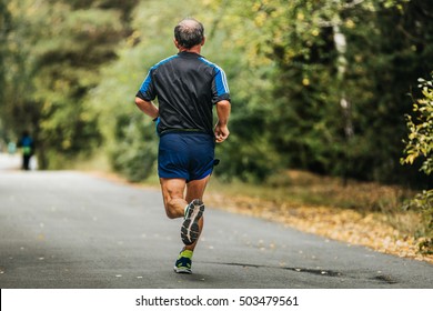 Active Elderly Man Running Down Road In Autumn Park