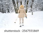 Active elderly woman with walking sticks exploring serene winter park with snowy paths. Outdoor winter activity, woman with walking sticks strolling through snowy landscape