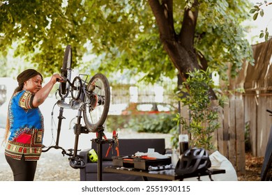 Active and energetic african american lady repairs and maintains bike components outside using professional equipment. Enthusiastic female cyclist carefully examining and fixing damaged bicycle. - Powered by Shutterstock