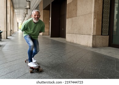 Active energetic happy cool gray haired old adult man skateboarding on city street, smiling sporty fit middle aged mature older male professional skater having fun enjoying riding skateboard outdoor.