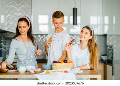 Active Family Of 3 People, Middle Age Good Looking Mother, Female Daughter And Teenage Son Have Fun Cooking Eating Together At Modern Kitchen. Family Gathering On Funny Party At Home.