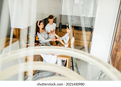 Active Family Of 3 People, Middle Age Good Looking Mother, Female Daughter And Teenage Son Have Fun Cooking Eating Together At Modern Kitchen. Family Gathering On Funny Party At Home.