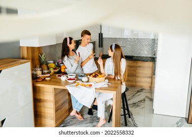 Active Family Of 3 People, Middle Age Good Looking Mother, Female Daughter And Teenage Son Have Fun Cooking Eating Together At Modern Kitchen. Family Gathering On Funny Party At Home.