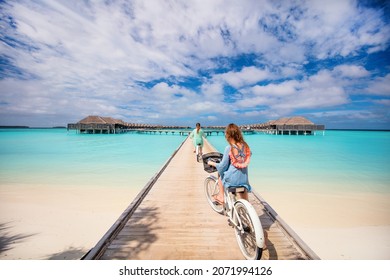 Active family of mother and daughter riding bikes on wooden jetty over tropical ocean enjoying tropical vacation