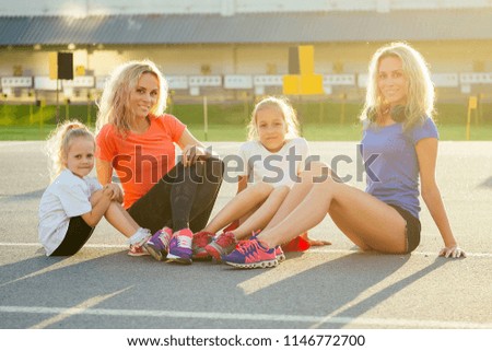 active family at outdoor. two blonde twin sisters mother and their daughters in stylish sportswear resting sitting on the asphalt in the stadium . group of four girls in the park
