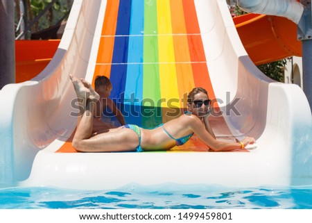 active family rest in the water park.The woman having fun in pool aqua park . slender blonde woman slide down on water slide.happy mother and son sunbathes by the pool in sunny days