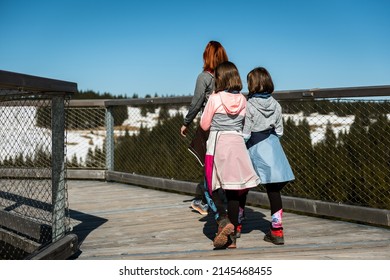 Active family walking, hiking in nature on wooden treetop walkway in winter. Family with kids walking mountain treetops on wooden balcony footbridge over the forest on Rogla, Pohorje, Slovenia.