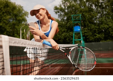 Active, fit and happy female tennis player browsing social media on her phone outdoors on the court. A young female athlete or sportswoman posting her sport training online or on the internet - Powered by Shutterstock