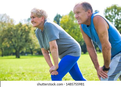 Active Flexible Senior Couple Stretching Leg In Park On Sunny Day