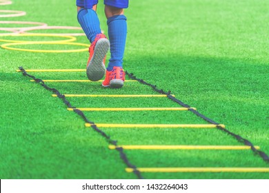 Active Football Child feet with soccer boots training on agility speed ladder in green soccer training ground.