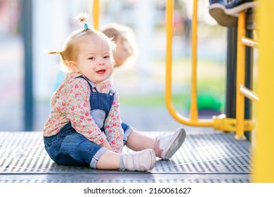 Active games for children. The kid is learning to climb stairs. Funny girl with pigtails on a children's slide. Happy child is playing on the playground. Baby has multi-colored short pigtails.