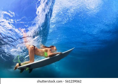 Active girl in bikini in action. Surfer woman with surf board dive underwater under breaking big wave. Healthy lifestyle. Water sport, extreme surfing in adventure camp on family summer beach vacation