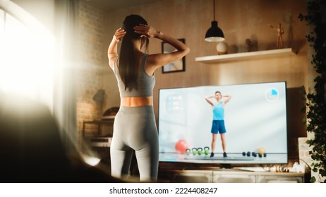 Active Girl Watching Personal Trainer Through Online Video Tutorial While Training At Home. Strong Athletic Fit Woman Streaming Fitness For Virtual Training Workout Service. Back View